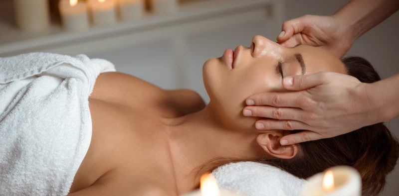 Young beautiful brunette girl having face massage relaxing in spa salon. Eyes closed. Copy space.